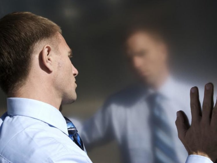A man looking at his reflection with hands touching the mirror