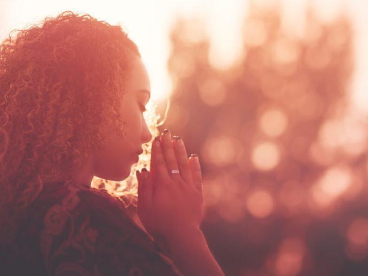 Young woman praying in view of a sunset