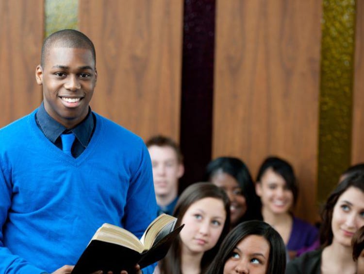 Young male pastor holds bible in full classroom