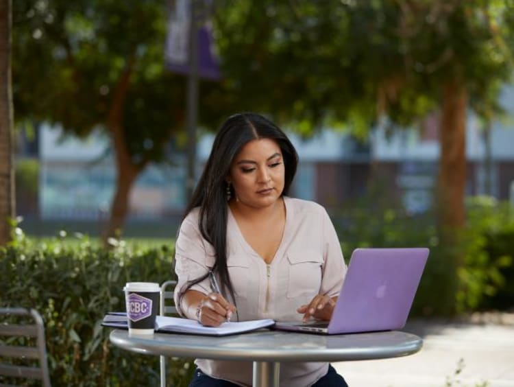 Doctoral student takes notes from laptop outdoors at GCU campus