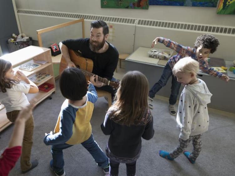 Man playing guitar with little kids around him