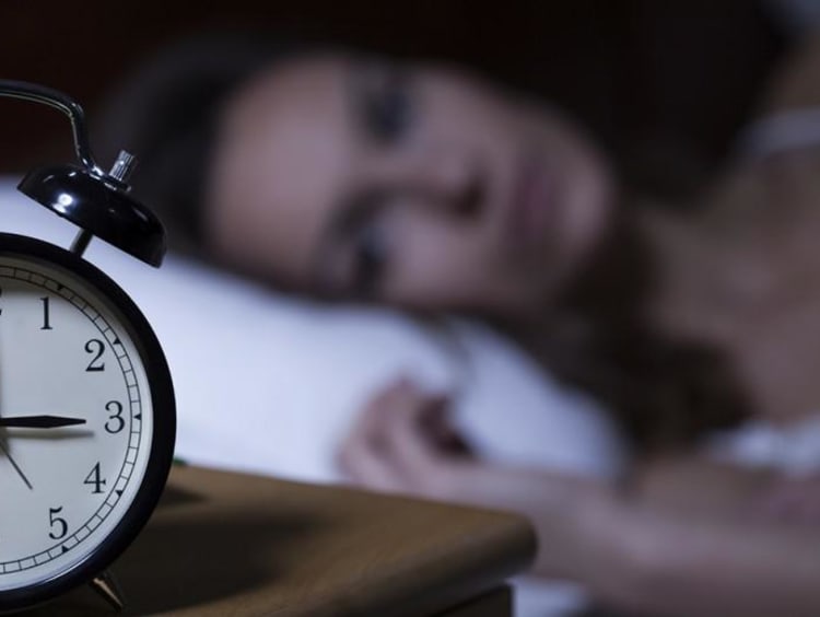 woman laying in bed looking at alarm clock