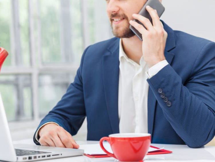 Adult man talks on cellphone sitting at a counter with a laptop