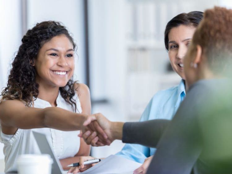 Small group of people shake hands and discuss at a table.