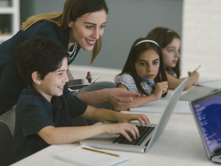 Female teacher helping young children navigate technology