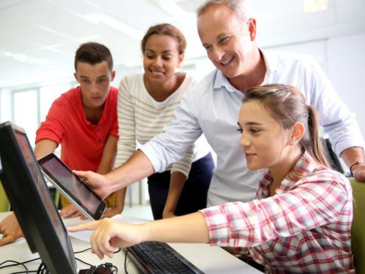 girl pointing to a computer and three other people watching