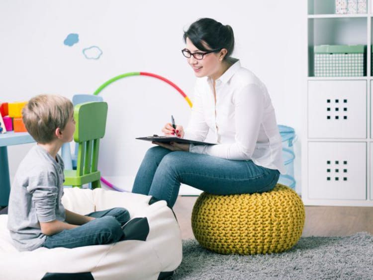 A family therapist sits in playroom and asks a little boy questions