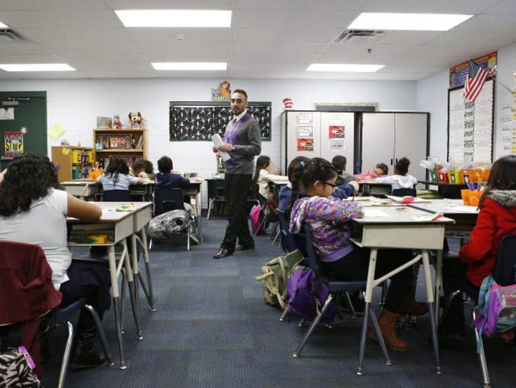 Hispanic male teacher paces classroom while students work