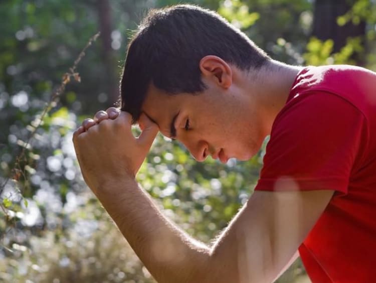 A man hanging his head in the wilderness