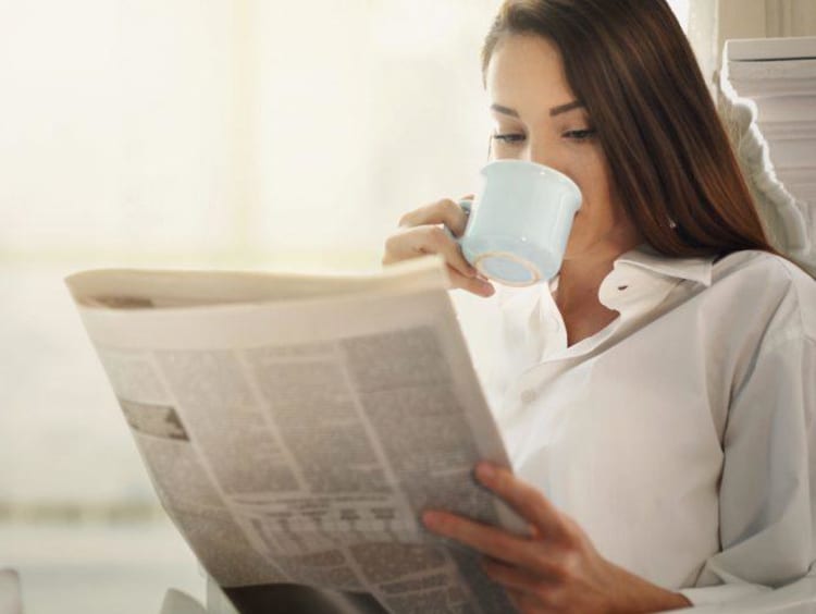 girl reading newspaper and sipping out of a mug