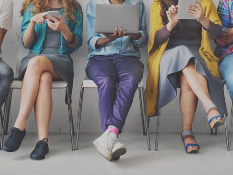 Front view of millennials sit in a row using phones and tablets