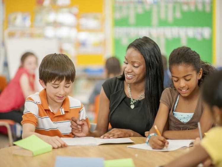 female teacher helping two young students in classroom