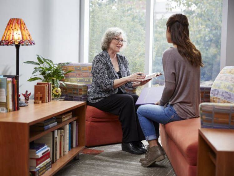 Older woman shares Bible reference with younger female sitting across from her