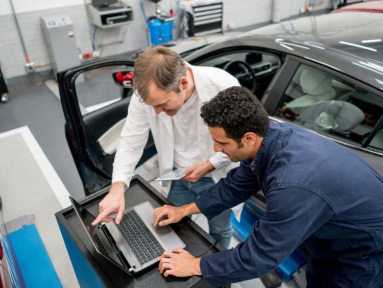 Man working on a computer by a car