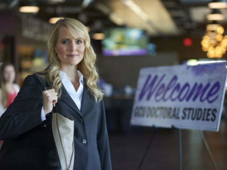 Blonde woman in professional clothing stands at entrance for doctoral studies mixer