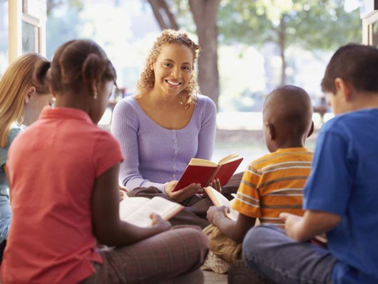 Teacher reads aloud to students sitting on the ground