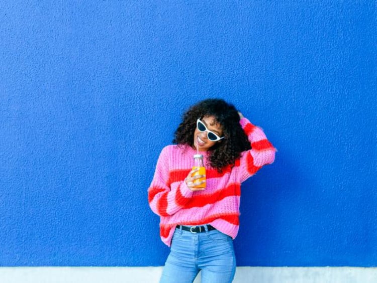 a girl sitting against a wall and drinking orange juice
