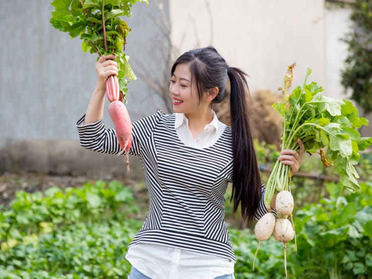 girl in a garden holding up two different vegetables