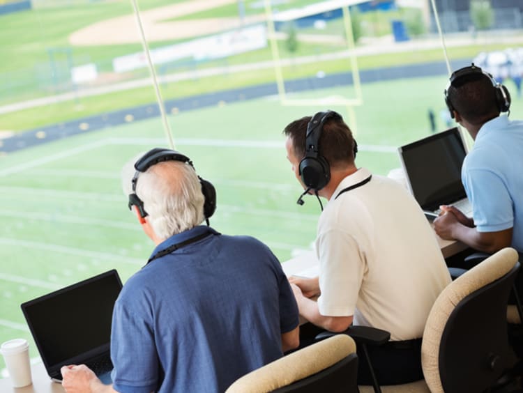 Three news broadcasters sitting side by side in sports stadium