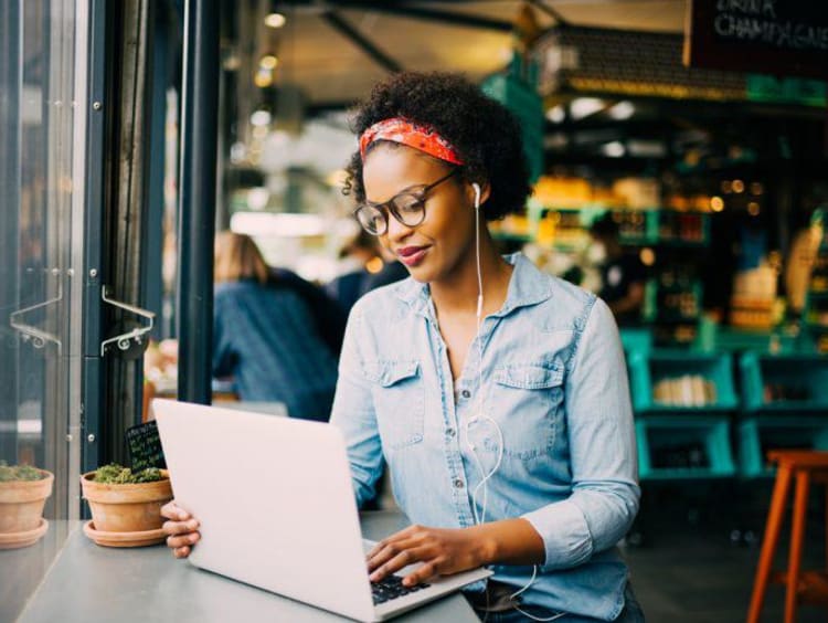 African-american women in a jean material long sleeved shirt with afro held up by red bandana uses laptop in a coffee shop