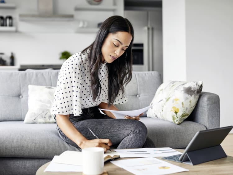 Woman sitting on gray couch in professional wear working on finances at home