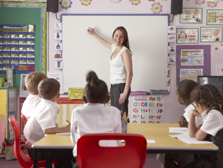 A group of diverse students learning from a teacher at a whiteboard