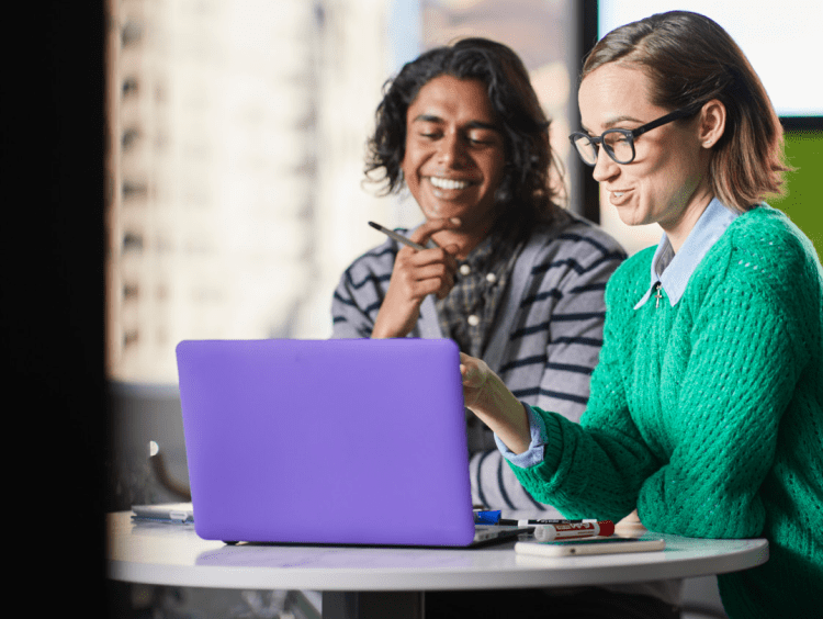 Two students work at laptop in office setting