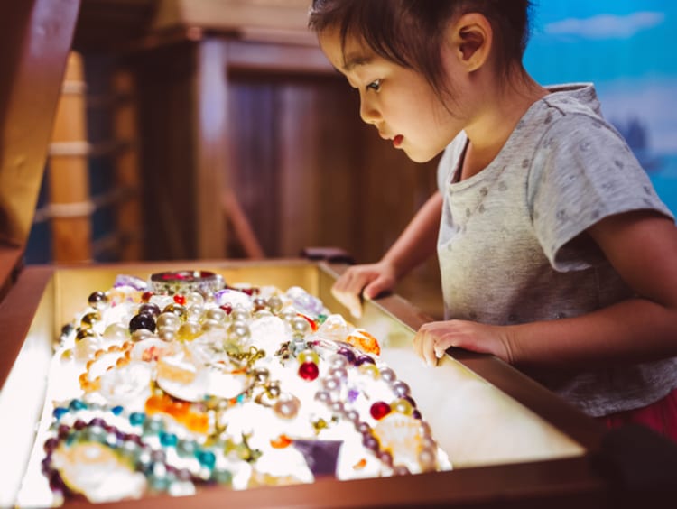 Little girl looking at pearls and other jewelry treasure in a chest
