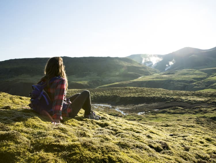 Woman sits on a grassy hill overlooking other grassy hills