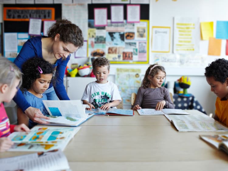 A group of elementary students reading books together with their teacher