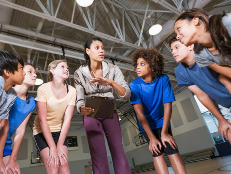 A PE teacher in a huddle with a group of her students