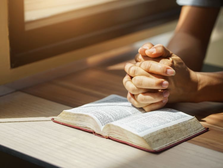 Praying hands rest on an open bible
