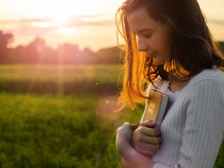 Young woman clutches Bible as the sun sets