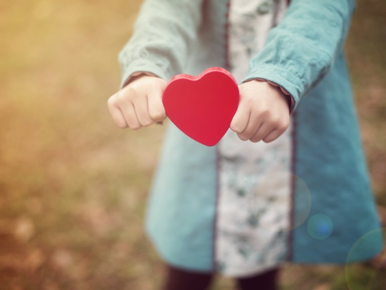 Woman holds out a cutout in the shape of a red heart