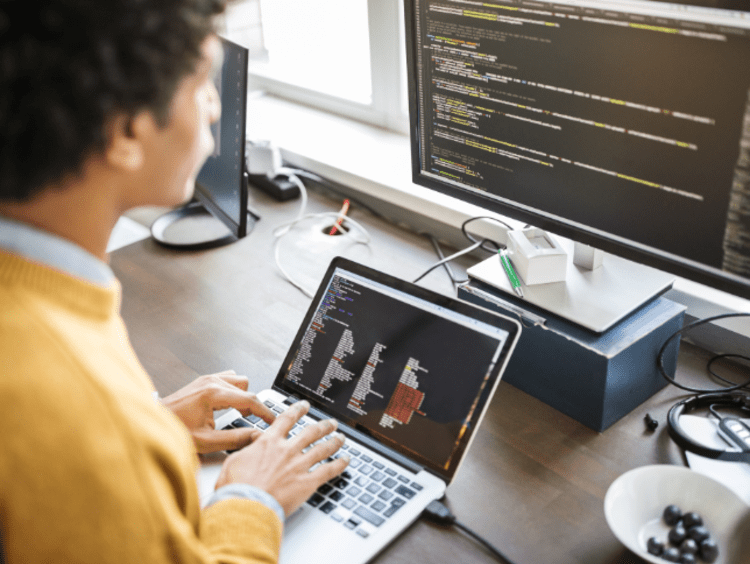 Man looking at two computer screens with code 