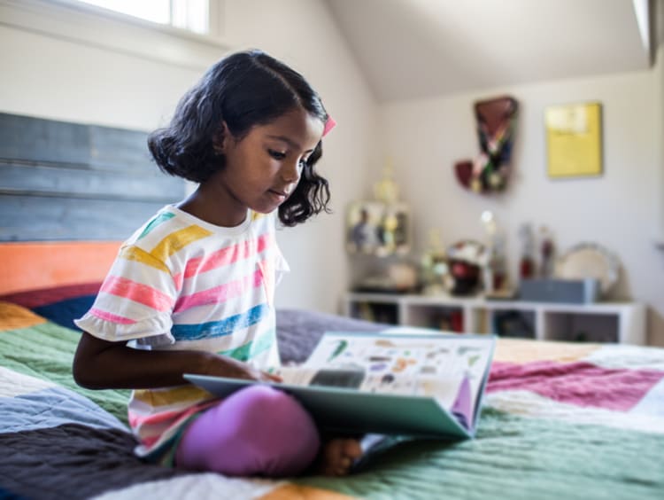 a child reading a book on her bed