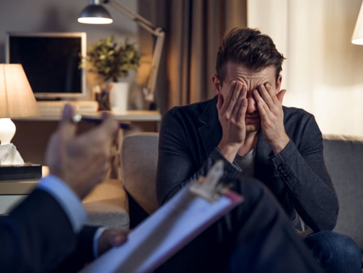 Man in suit with face in hands sitting across from woman counselor