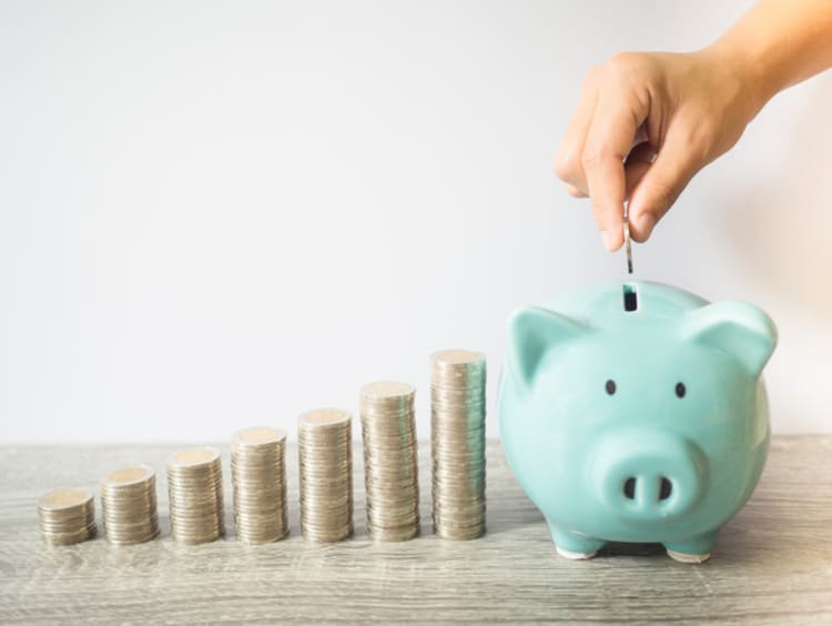 putting coins in a piggy bank next to stacks of coins