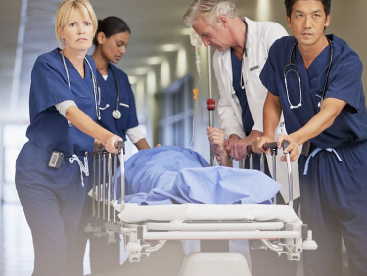 Two female nurses and one male nurse wheeling patient on cart with doctor