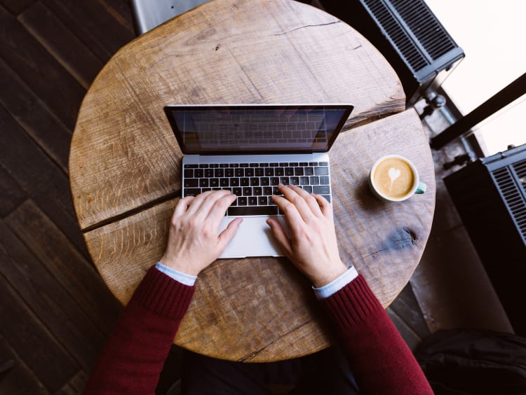 Typing on laptop with coffee next to it in a cafe