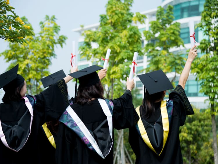 four college grads in their cap and gowns holding diplomas