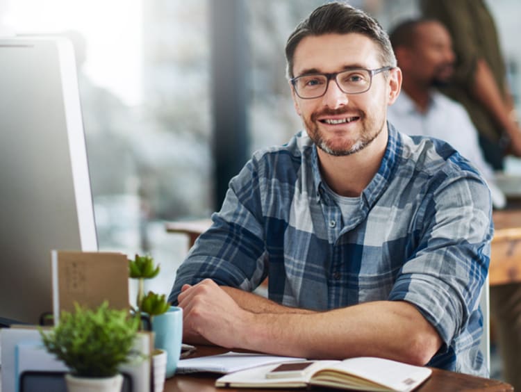 mba candidate sitting at his desk with colleagues in the background