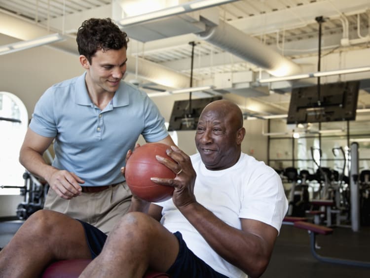 physical therapy assistant helping a patient lift a ball