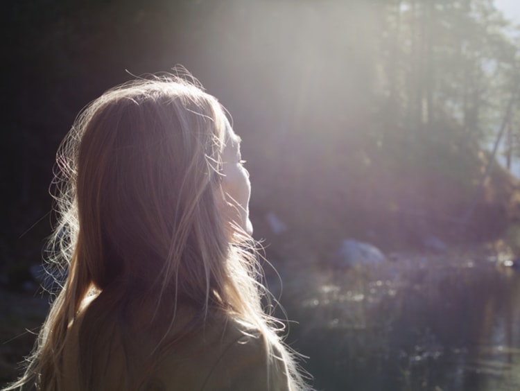 Blonde woman faces sunlight at lake shore