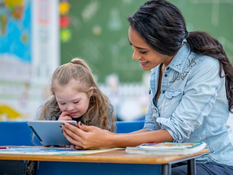 Female teaching assistant working with young student in classroom