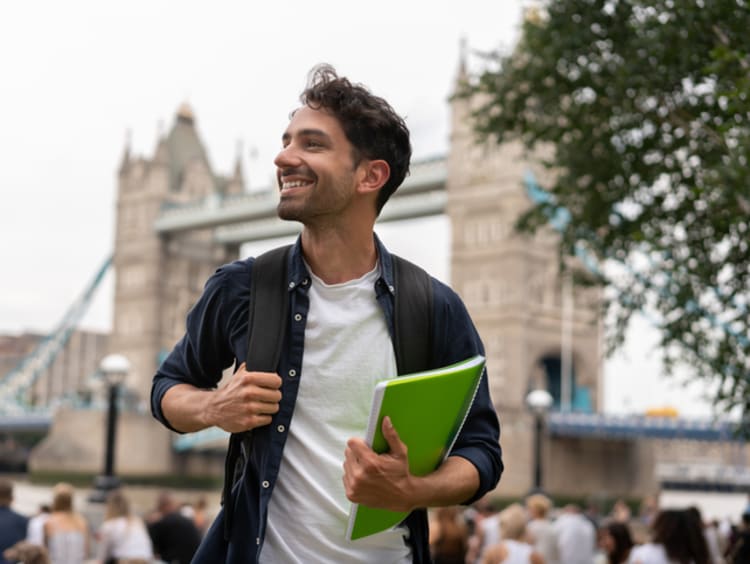 Young man in a foreign city holding a notebook and backpack