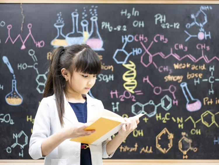 girl in lab coat using picture book for science class