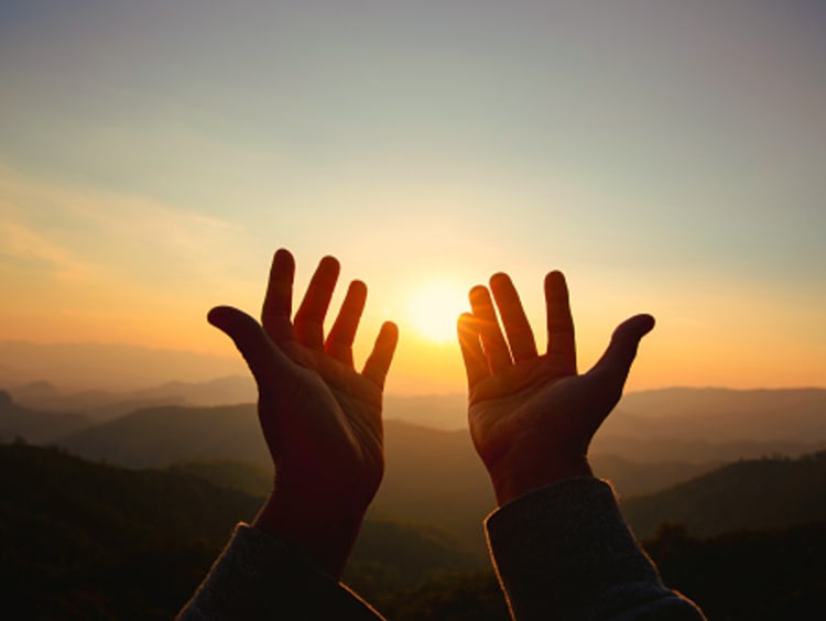 Hands raised to a sunrise sky