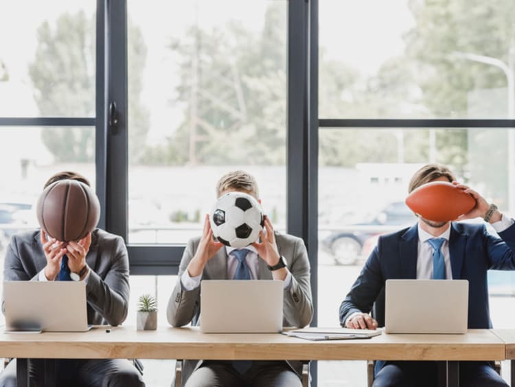 Three office workers holding different sports balls in their hands