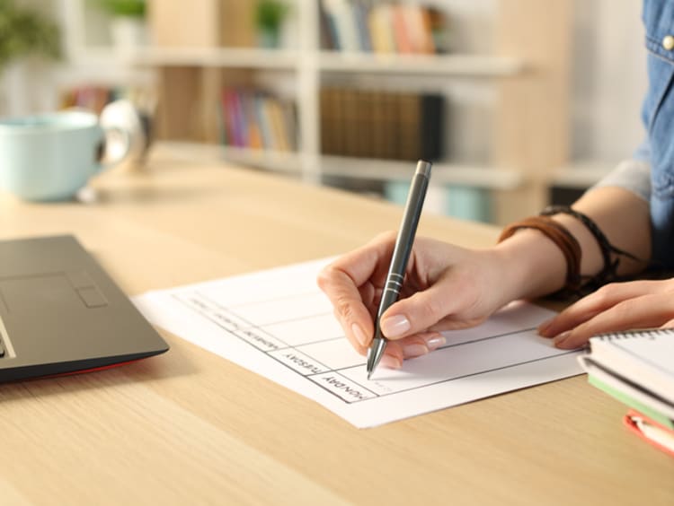 Student at a desk with laptop planning out their tasks on a paper calendar